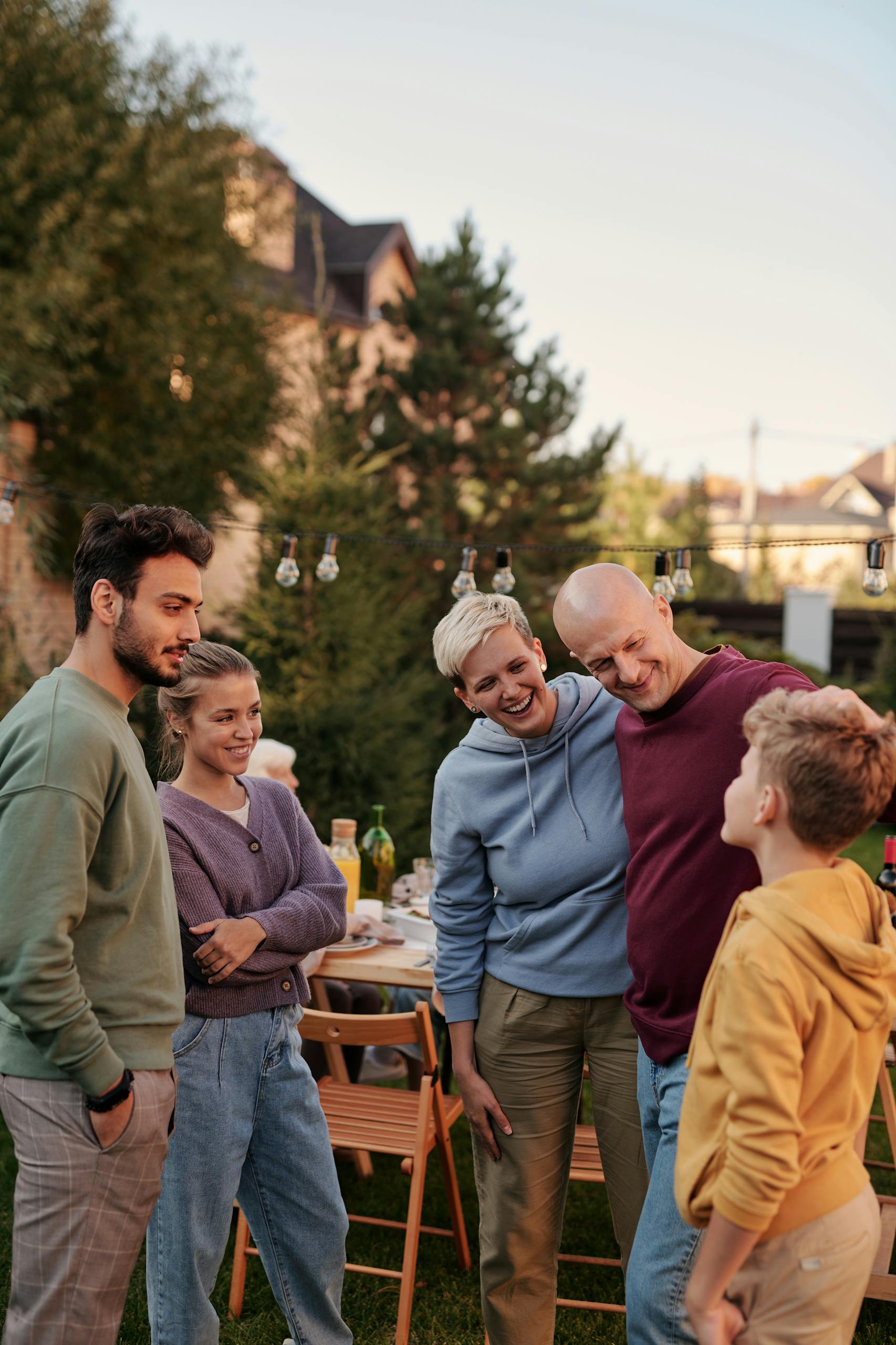 Group of family members smiling and chatting in a backyard setting during a summer evening.